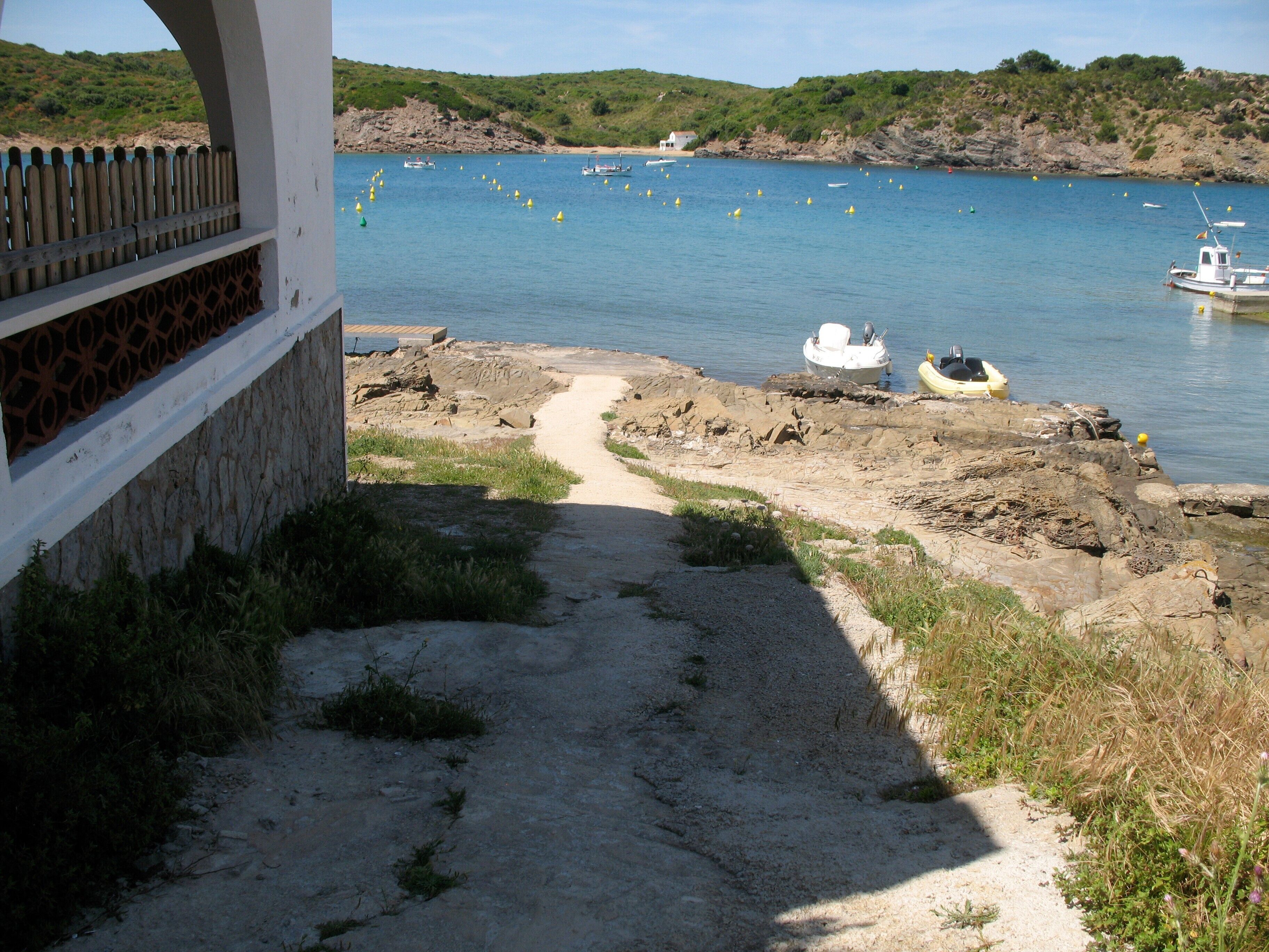 A coastal path leading to a rocky beach with boats and buoys in the water.