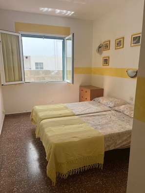 Una habitación con dos camas, una ventana, una repisa en la pared y una puerta.