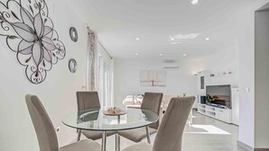 Un salon moderne avec une table à manger en verre, des sièges confortables, un téléviseur à écran plat et des œuvres d’art décoratives au mur.