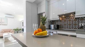 Une cuisine moderne avec des armoires blanches, un four à micro-ondes encastré et un panier de fruits sur l’îlot central.
