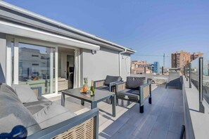 A rooftop terrace with outdoor seating, a table with drinks, and a view of the cityscape.