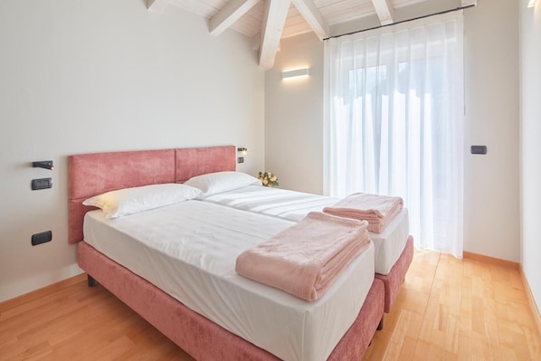 Un lit double avec une tête de lit rose, une literie blanche et une serviette rose posée sur le pied de lit.