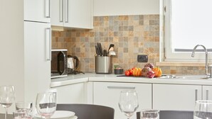 Una cocina moderna con armarios blancos, salpicadero de azulejos y un comedor dispuesto con platos, vasos y cubiertos.