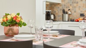Una mesa de comedor dispuesta con platos, vasos y un jarrón de flores.