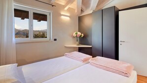 Un dormitorio con dos camas, una ventana con vistas a la montaña, un florero con flores y un armario oscuro.