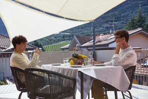 Deux personnes dînent à une table en plein air, avec vue sur les vignes, à l’abri d’une tonnelle.