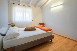 A bedroom with a bed, a window with curtains, a bedside table, and a wall-mounted light.