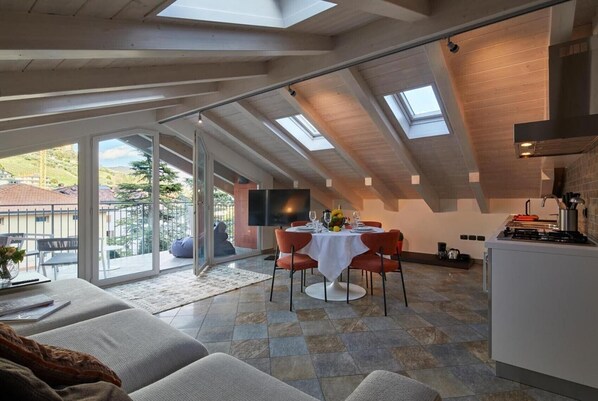 A modern loft with a dining area, kitchen, and large sliding glass doors leading to a balcony.