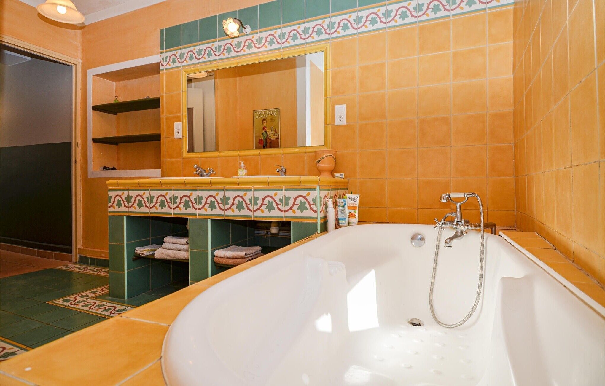 Ein Badezimmer mit einer großen Badewanne, einem Waschtisch inklusive Spiegel und einem gefliesten Boden.