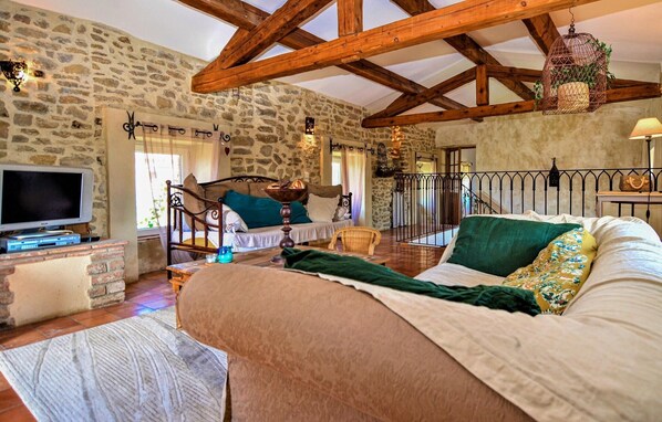 A rustic room with exposed stone walls, wooden beams, a bed with pillows, a TV, and a small table with a lamp.