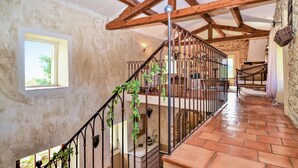 Una escalera con barandilla de hierro forjado, una pared de piedra y una ventana con vista a follaje.