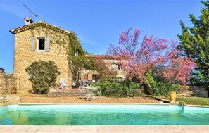 A stone building with a swimming pool, outdoor furniture, and flowering trees.