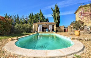 Ein Pool mit Stein оформлением, eine überdachte Außenlounge und ein Gebäude mit Steinwänden und einem Ziegeldach.