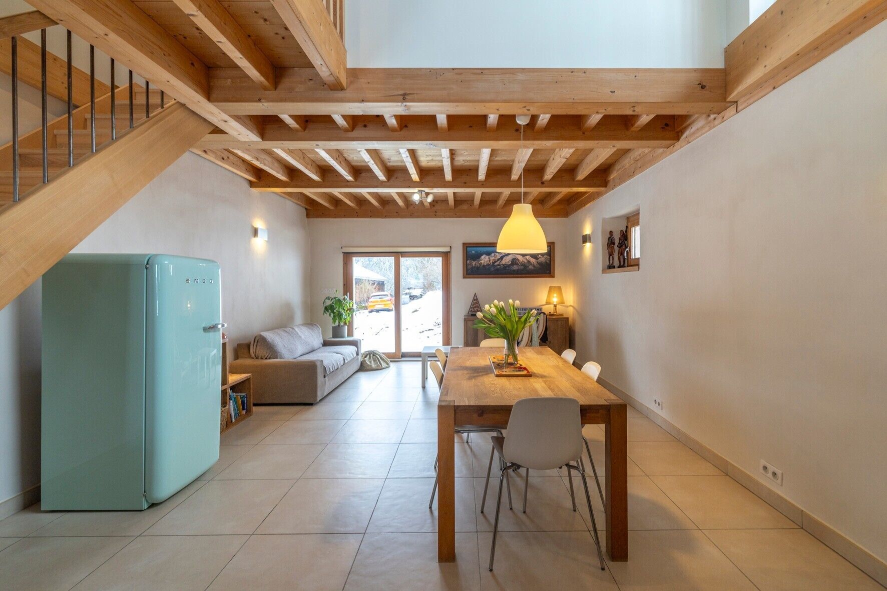 Een modern interieur met een houten wenteltrap, een zithoek met tafel en stoelen, een bank en een blauwe koelkast.