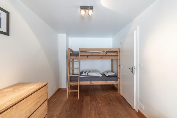 A bunk bed room with a wooden dresser and a door.