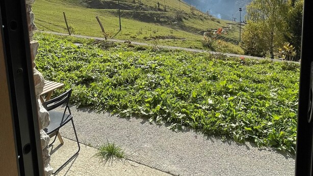Une vue sur un vignoble, avec une chaise et une table au premier plan, une chaîne de montagnes en arrière-plan et un ciel dégagé.