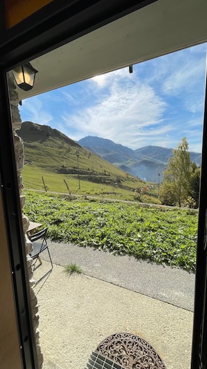 Blick auf ein Weinberg mit Stuhl und Tisch im Vordergrund, einem Gebirge im Hintergrund und blauem Himmel.