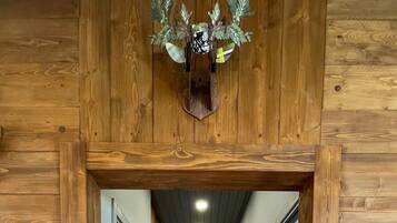 Un couloir en bois avec un luminaire fixé au plafond, une porte au fond et un téléviseur fixé au mur sur la droite.