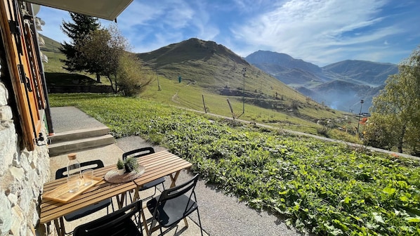 Eine Terrasse mit Tisch und Stühlen, die auf ein Tal mit Bergen und einem See blickt.