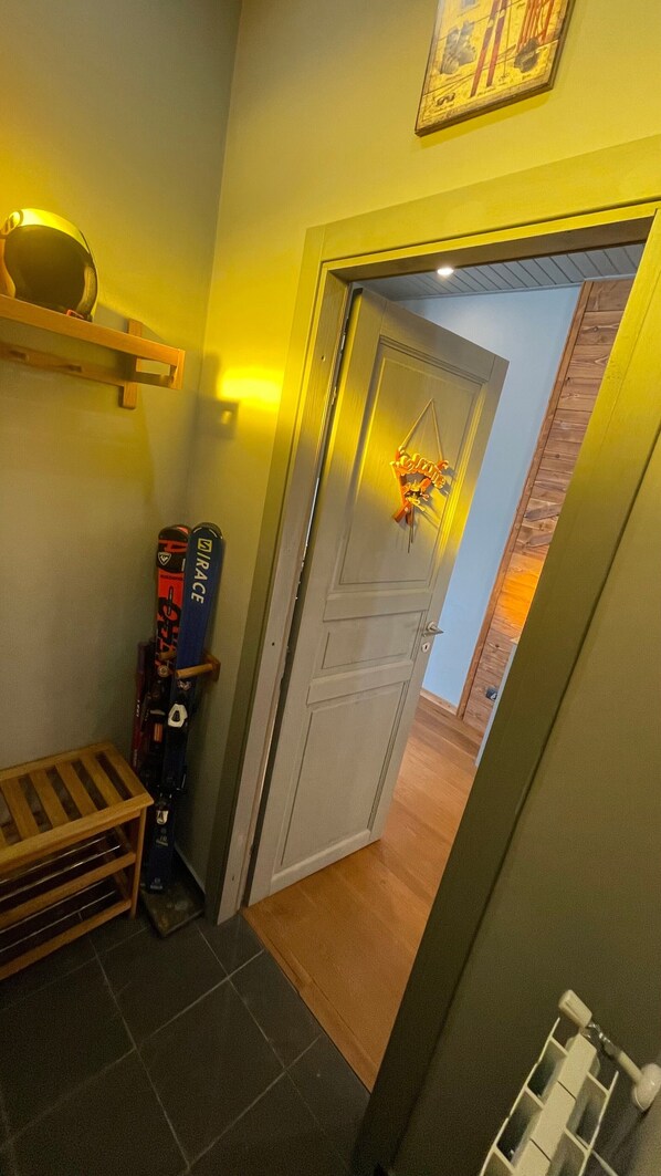 A hallway with a wooden bench, skis leaning against the wall, and a door leading to another room.