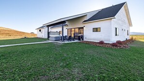 A modern single-story house with a covered patio, a lawn, and a view of the countryside. - Elk Run Ranch With Hot Tub (Tetonia)