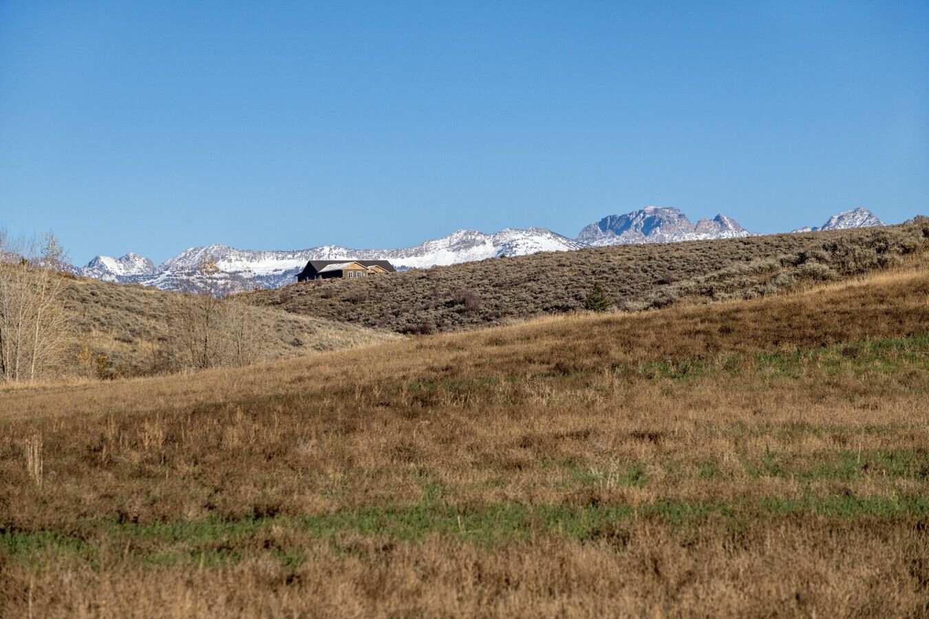 Ländliche Landschaft mit einem Haus auf einem Hügel, umgeben von Bergen und vereinzelter Vegetation.