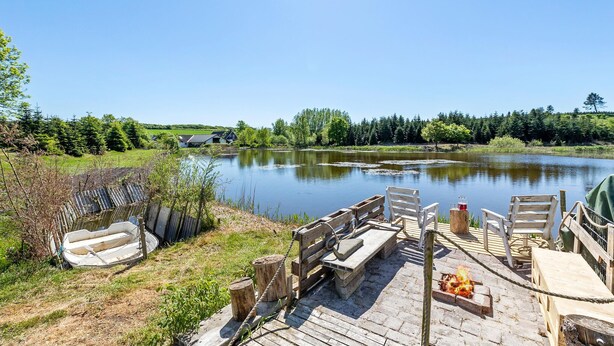 A wooden dock with benches and a fire pit, overlooking a calm lake with a forested background. - Beautiful home in Nibe with sauna (Nibe)