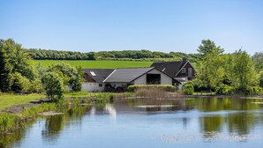 A house with a large barn, a pond, and a green field in the background. - Beautiful home in Nibe with sauna (Nibe)