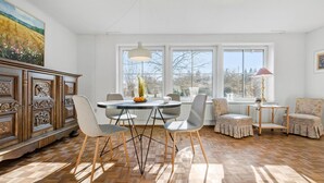 A dining area with a round table, chairs, and a view of trees through large windows. - Beautiful home in Nibe with sauna (Nibe)