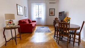 A living room with a red sofa, a wooden dining table with chairs, a TV, and a window with curtains. - Elegantis Solinda Suite Apartment with Private Terrace - Metro, Tram & Bus (Roma)