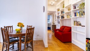 A dining area with a wooden table and chairs, a red sofa, and a white bookshelf filled with books and decorative items. - Elegantis Solinda Suite Apartment with Private Terrace - Metro, Tram & Bus (Roma)
