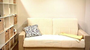 A neutral-colored sofa with a patterned pillow and a blanket, a white shelving unit with wicker baskets, and a wooden floor. - Cozy suite ideally located for visiting major sights (Bari)