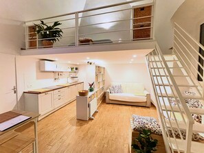 Un vaste espace de vie doté d’un haut plafond, une cuisine avec des meubles blancs, une table à manger et un escalier avec une rampe.