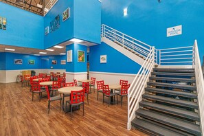 A blue-walled indoor pool area with red chairs and tables, a staircase, and a sign indicating the indoor pool location.