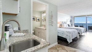 A hotel room with a kitchen area, a bathroom, and a balcony with a view.