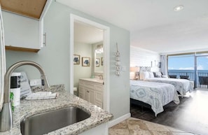 A hotel room with a kitchen area, a bathroom, and a balcony with a view.