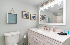 A bathroom with a toilet, a sink with a mirror, and framed artwork on the wall. - Sand Dunes 2542 (Myrtle Beach)