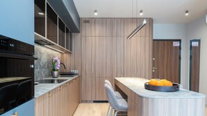 A modern kitchen with wooden cabinets, a marble countertop, and a built-in oven. There are two bar stools and a fruit bowl on the counter. - Cracow Superior Apartment (Kraków)