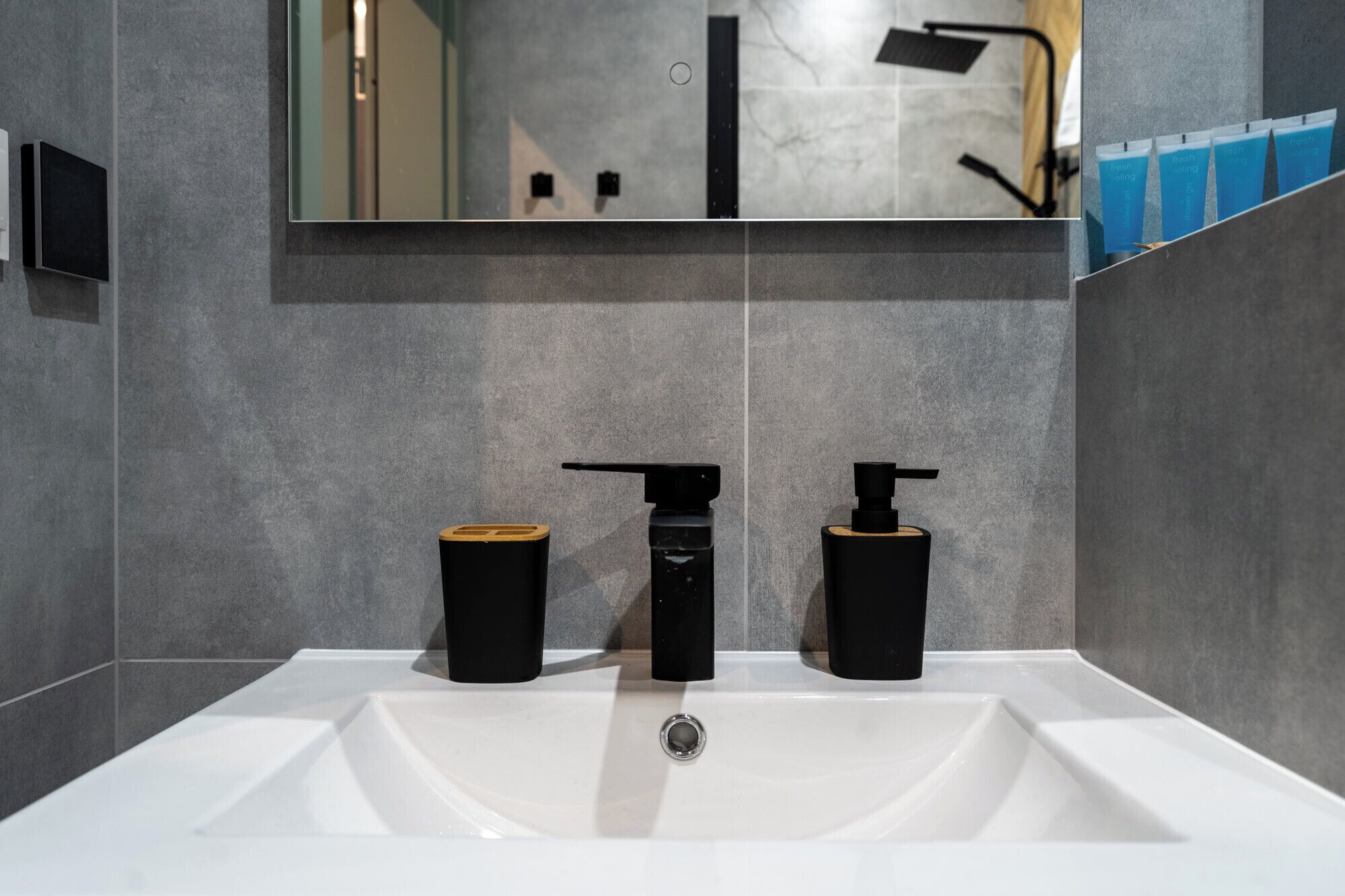 A modern bathroom with a white sink, two black dispensers, and a wooden soap holder.