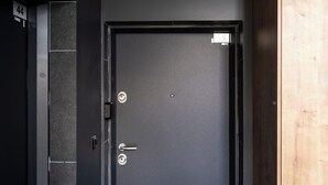 Een zwarte deur met een handgreep en slot, een klein bord erboven en een houten paneel aan de rechterkant.