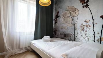 A bedroom with a bed, a wall mural, a window with sheer curtains, and a hanging light fixture.