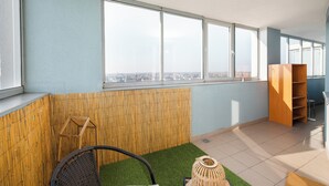 Una habitación moderna con ventanas amplias, un panel de bambú, una silla de mimbre, una pequeña zona verde y una estantería de madera.