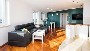 Una sala de estar moderna con un sofá de cuero negro, una mesa de centro blanca y una zona de comedor con una mesa y sillas blancas.