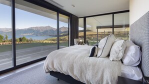 Ein modernes Schlafzimmer mit einem großen Bett, Blick auf Berge und einen See, und einem großen Fenster.