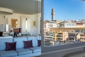 A modern living room with a sofa, a television, and a view of a historic cityscape with a prominent tower.
