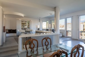 A modern interior with a central kitchen island, dining area, and large windows offering a view of the city.