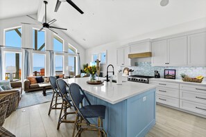 A modern kitchen with a large island, white cabinets, and a view to the outside.