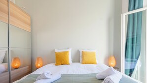 Una habitación de hotel con una cama grande, dos almohadas, un plaid verde y dos lámparas de noche.