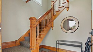 Eine Holztreppe mit Handlauf, ein runder Spiegel an der Wand und eine Metallbank.