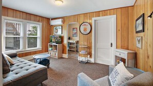Ein gemütliches Wohnzimmer mit einer Couch, einem Couchtisch und einem Fernseher. Im Hintergrund ist eine Holzwand und eine Tür zu sehen.
